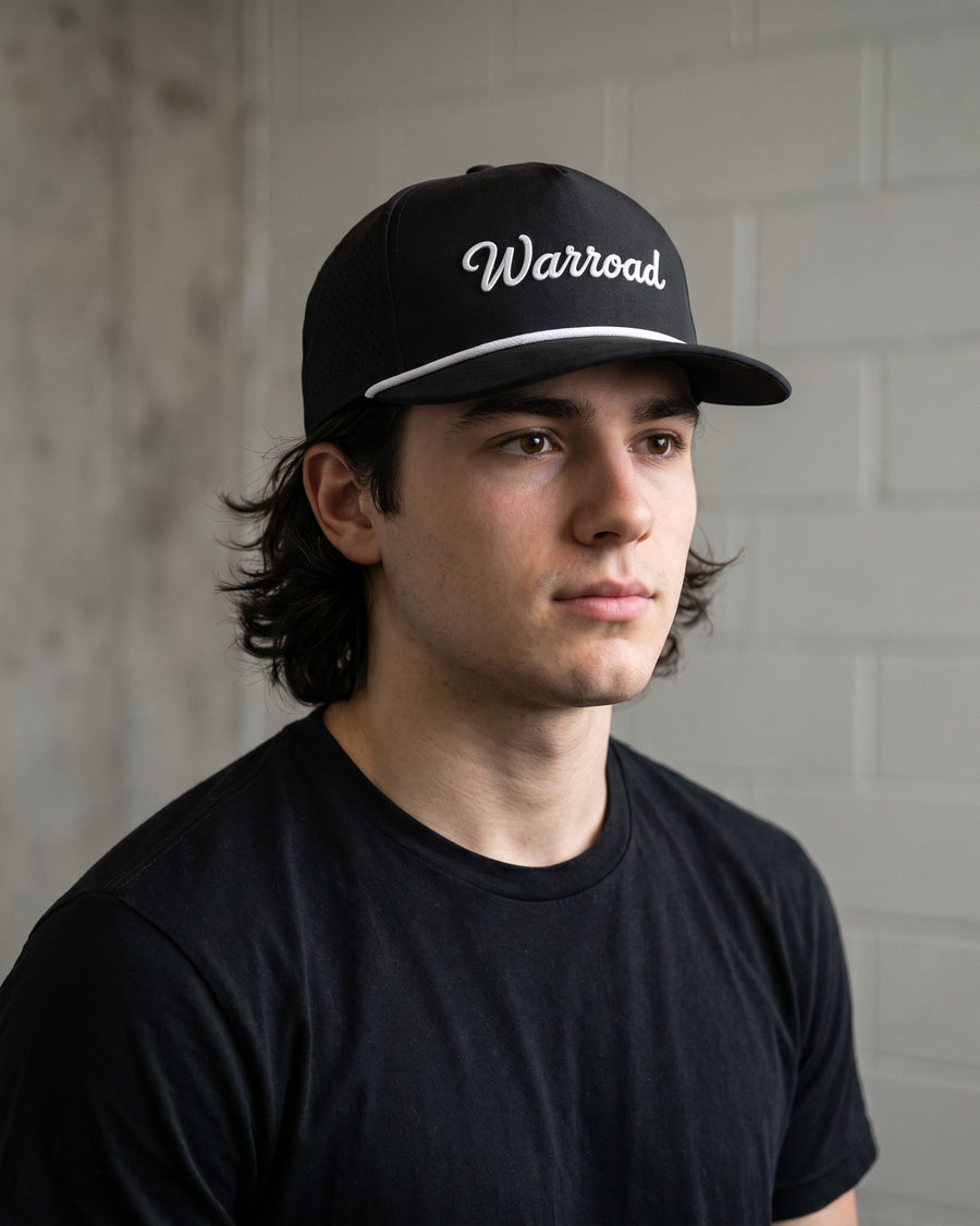 Lifestyle: Black Warroad Rope Hat worn outdoors, relaxed off-ice moment with the white Warroad cursive visible on the front. - image 6